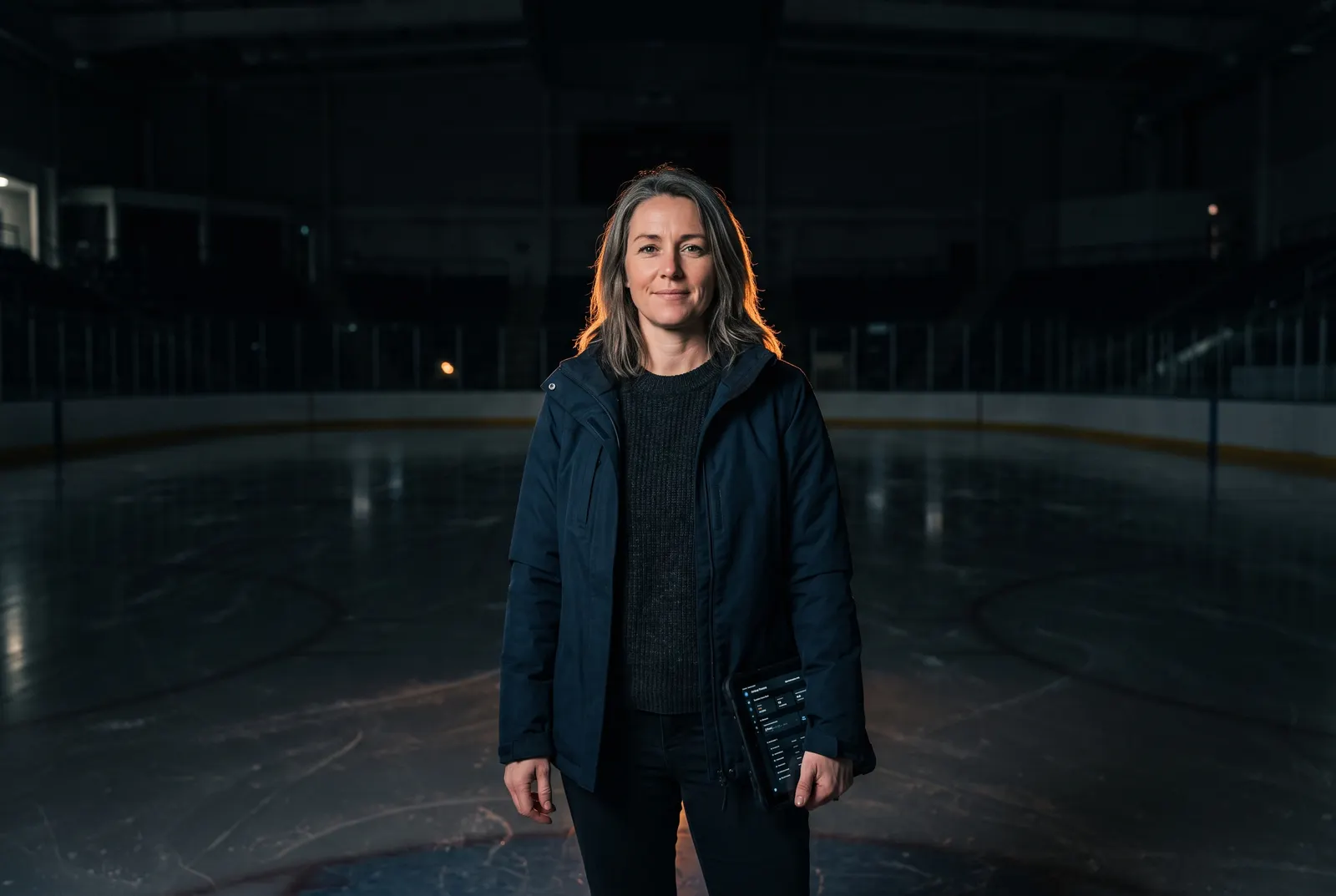 A club manager standing on the ice of an empty arena at night, holding a tablet.