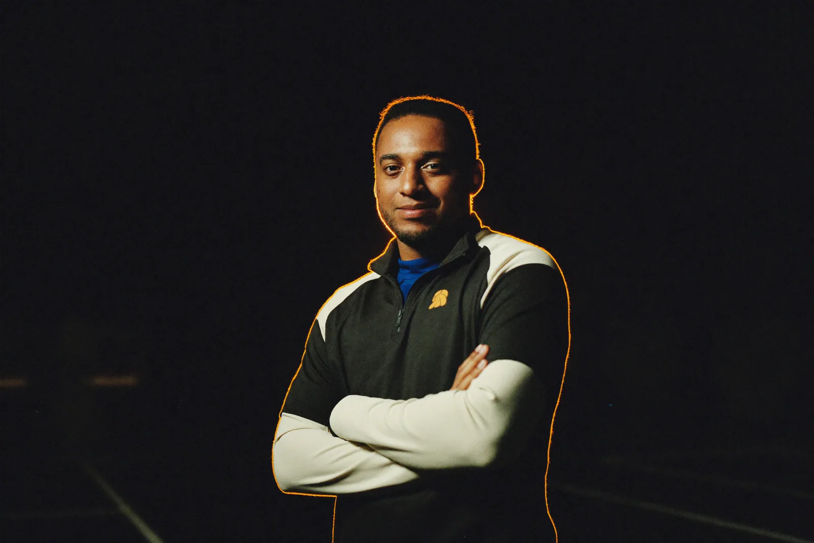 An editorial portrait of a confident sports coach, lit by a single warm rim light against darkness.