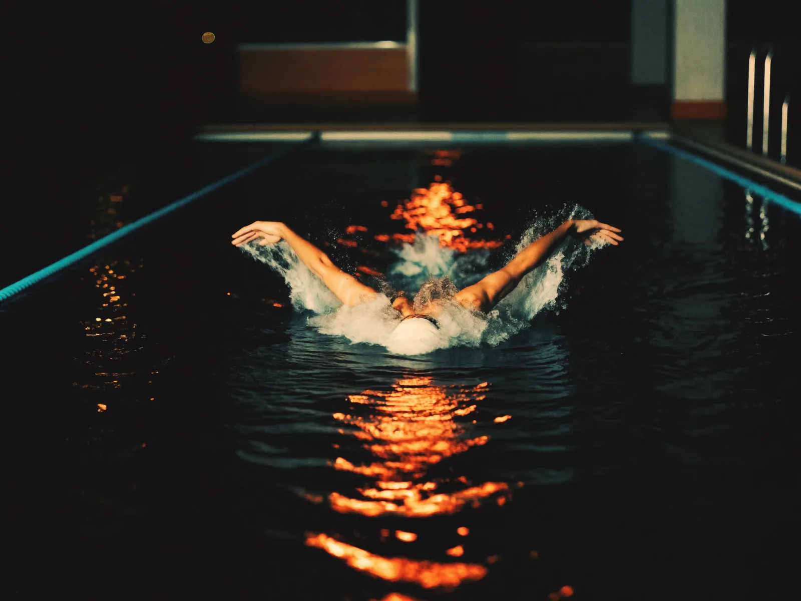 A swimmer powering through dark water, an orange light streak rippling across the surface.