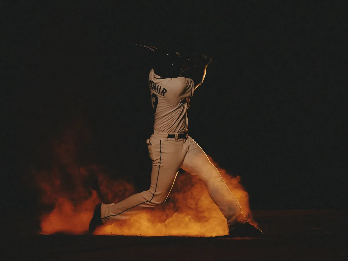 An adult baseball batter following through on a powerful swing at night.