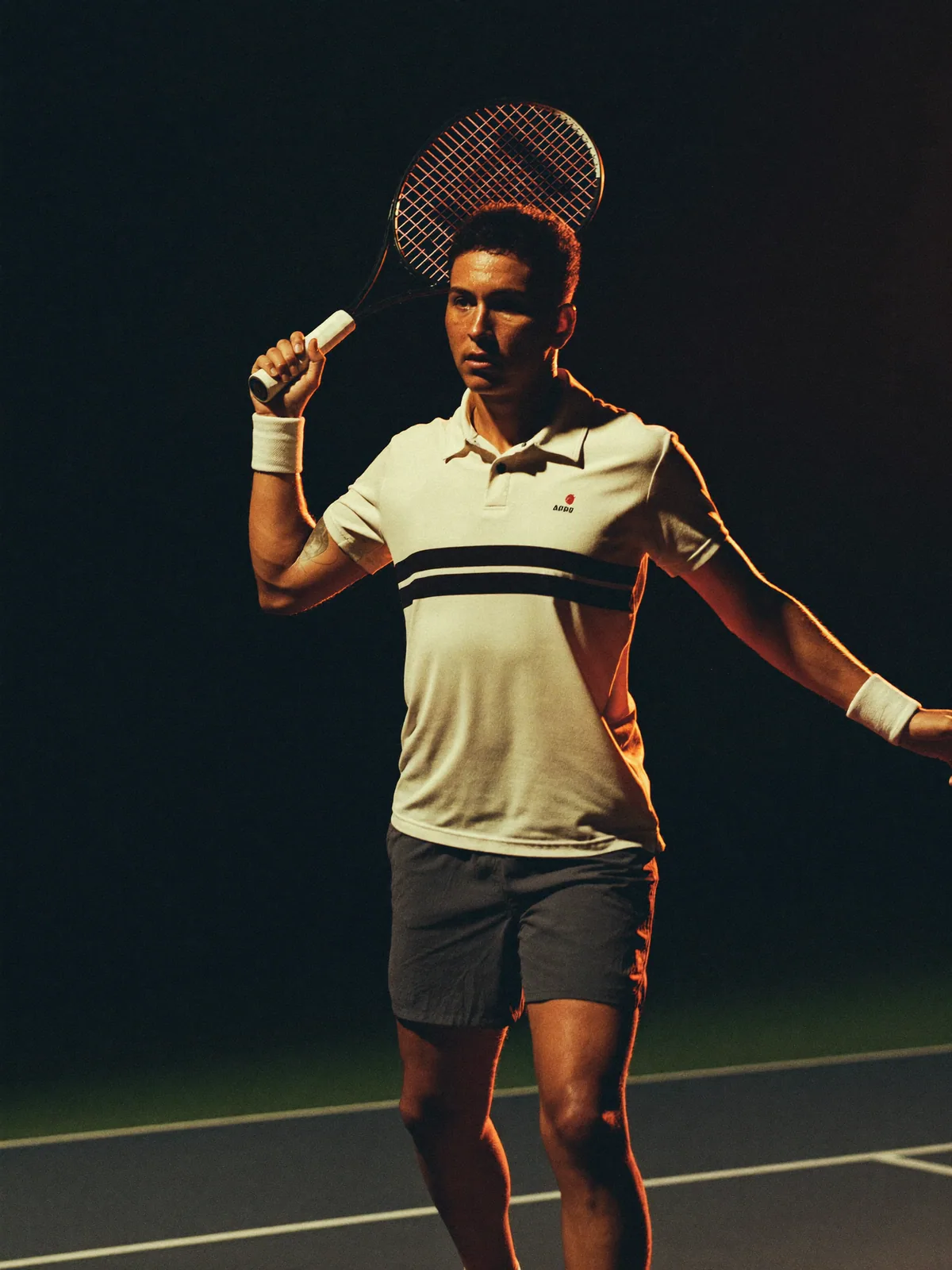 An adult tennis player following through on a forehand under court floodlights.