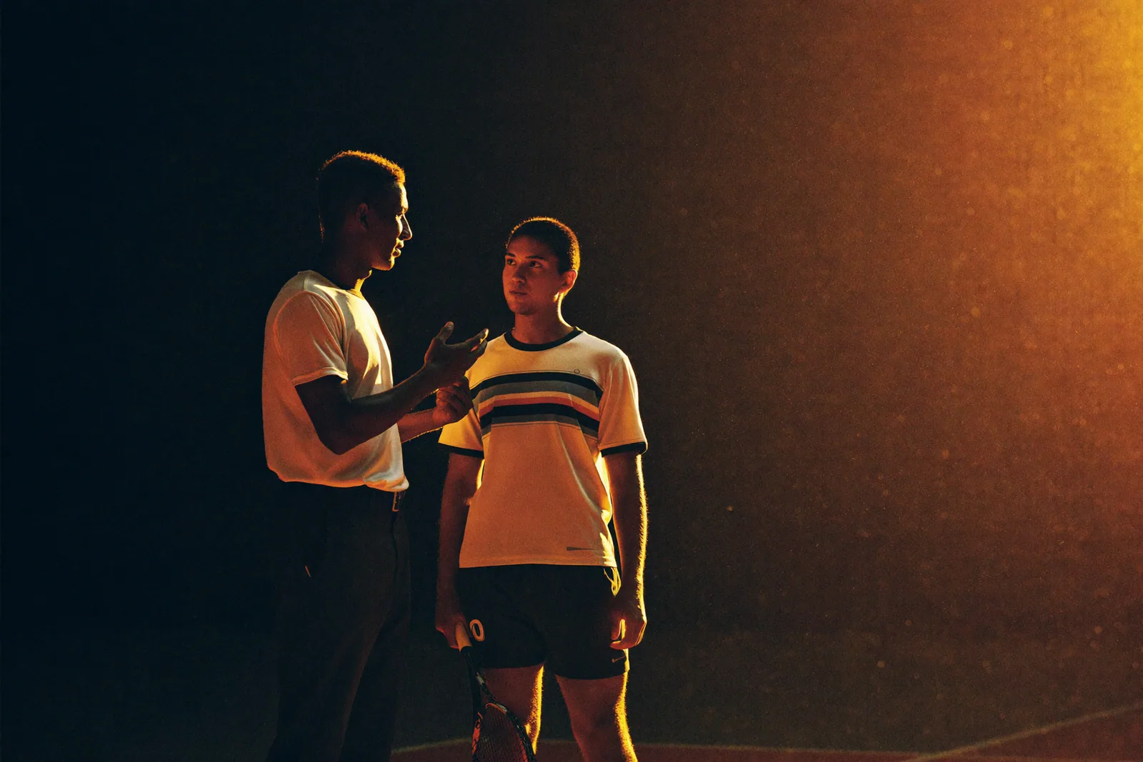 A coach reviewing technique with an adult athlete on a dark indoor court at night.